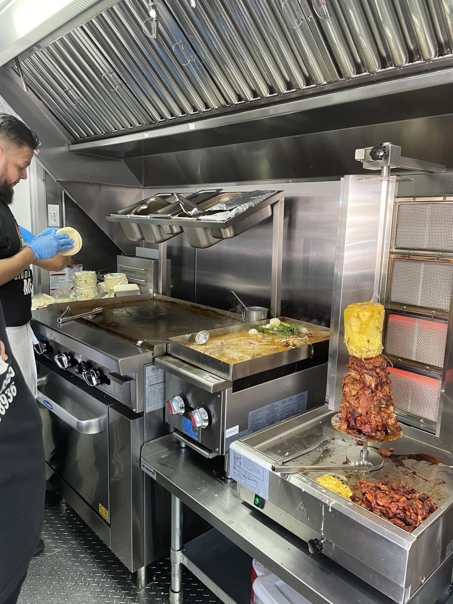 Al pastor cooking on a vertical spit next to a busy flat-top grill inside the truck